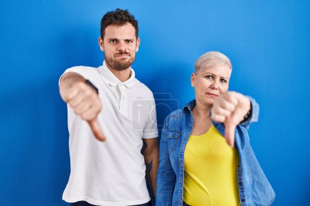 Photo for Young brazilian mother and son standing over blue background looking unhappy and angry showing rejection and negative with thumbs down gesture. bad expression. - Royalty Free Image