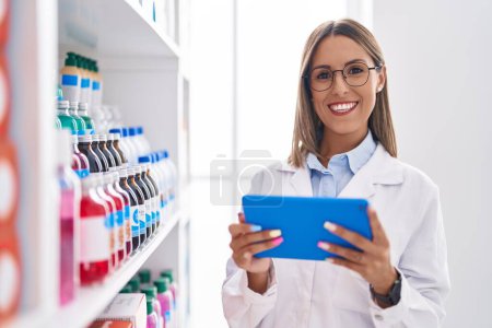 Photo for Young beautiful hispanic woman pharmacist using touchpad working at pharmacy - Royalty Free Image