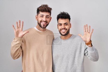 Téléchargez les photos : Jeune couple homosexuel debout sur fond blanc montrant et pointant vers le haut avec les doigts numéro dix tout en souriant confiant et heureux. - en image libre de droit