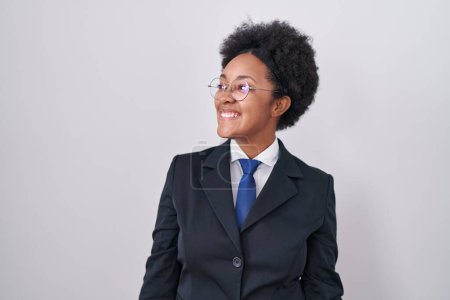 Téléchargez les photos : Beautiful african woman with curly hair wearing business jacket and glasses looking away to side with smile on face, natural expression. laughing confident. - en image libre de droit