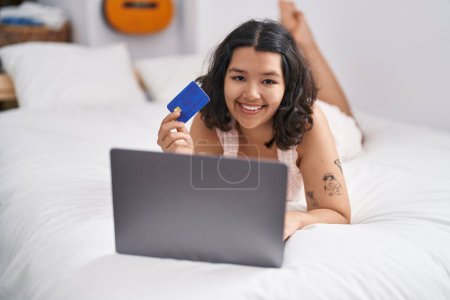 Foto de Mujer joven usando portátil y tarjeta de crédito acostada en la cama en el dormitorio - Imagen libre de derechos