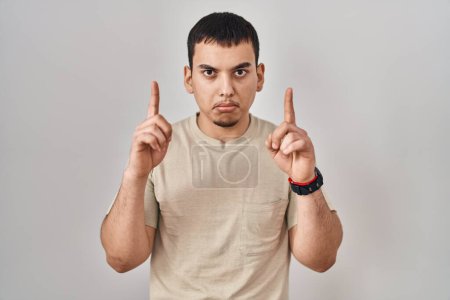 Foto de Hombre árabe joven con camiseta casual apuntando hacia arriba mirando triste y molesto, indicando la dirección con los dedos, infeliz y deprimido. - Imagen libre de derechos