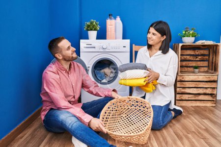 Téléchargez les photos : Jeune couple faisant la lessive à la maison souriant regardant vers le côté et regardant loin en pensant. - en image libre de droit