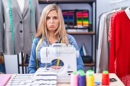 Photo for Blonde woman dressmaker designer using sew machine depressed and worry for distress, crying angry and afraid. sad expression. - Royalty Free Image