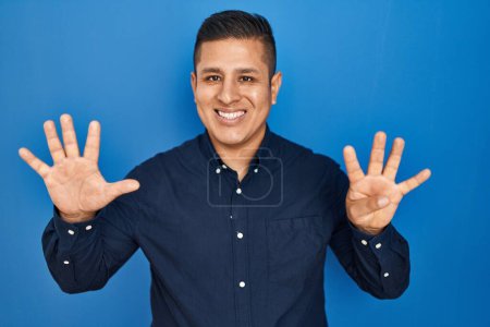 Téléchargez les photos : Jeune homme hispanique debout sur fond bleu montrant et pointant vers le haut avec les doigts numéro neuf tout en souriant confiant et heureux. - en image libre de droit