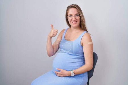 Photo for Young pregnant woman wearing band aid for vaccine injection smiling happy and positive, thumb up doing excellent and approval sign - Royalty Free Image