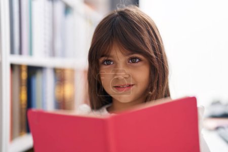 Téléchargez les photos : Adorable fille hispanique étudiant souriant livre de lecture confiant à la salle de classe - en image libre de droit