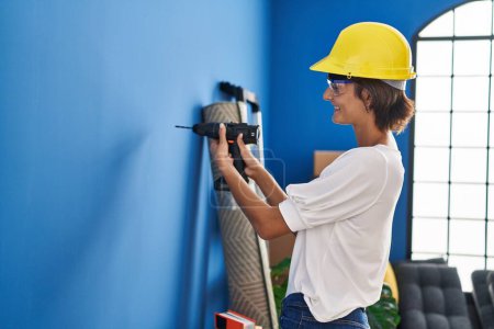 Photo for Young beautiful hispanic woman smiling confident drilling wall at new home - Royalty Free Image