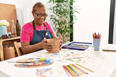 Foto de Mujer afroamericana mayor sonriendo confiada haciendo cerámica de arcilla en el estudio de arte - Imagen libre de derechos