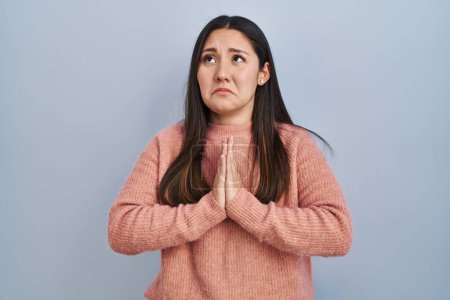 Photo for Young latin woman standing over blue background begging and praying with hands together with hope expression on face very emotional and worried. begging. - Royalty Free Image