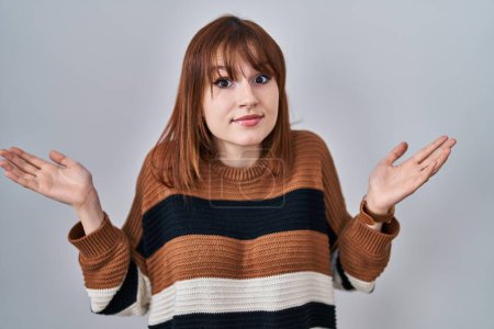 Téléchargez les photos : Young beautiful woman wearing striped sweater over isolated background clueless and confused expression with arms and hands raised. doubt concept. - en image libre de droit