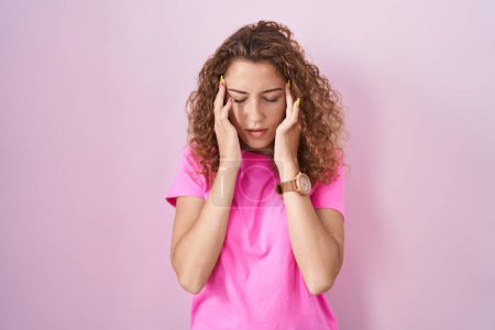 Foto de Young caucasian woman standing over pink background with hand on head, headache because stress. suffering migraine. - Imagen libre de derechos