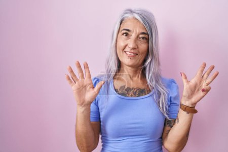 Téléchargez les photos : Femme d'âge moyen avec des tatouages debout sur fond rose montrant et pointant vers le haut avec les doigts numéro neuf tout en souriant confiant et heureux. - en image libre de droit