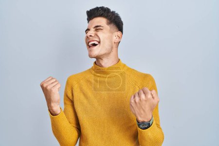 Photo for Young hispanic man standing over blue background celebrating surprised and amazed for success with arms raised and eyes closed. winner concept. - Royalty Free Image