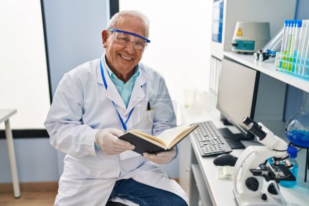 Photo for Senior man wearing scientist uniform reading book at laboratory - Royalty Free Image