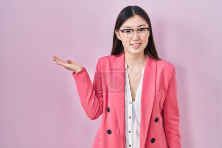 Téléchargez les photos : Chinois entreprise jeune femme portant des lunettes souriant joyeuse présentation et pointant avec la paume de la main en regardant la caméra. - en image libre de droit