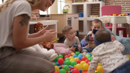 Photo for Teacher and preschool students playing with balls and cars sitting on floor at kindergarten - Royalty Free Image