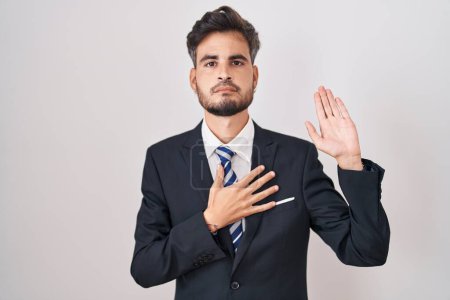 Photo for Young hispanic man with tattoos wearing business suit and tie swearing with hand on chest and open palm, making a loyalty promise oath - Royalty Free Image