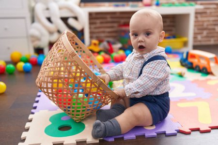 Foto de Adorable bebé caucásico jugando con bolas sentadas en el suelo en el jardín de infantes - Imagen libre de derechos