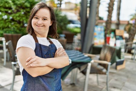 Téléchargez les photos : Jeune femme trisomique souriant avec confiance portant tablier à la terrasse du café - en image libre de droit