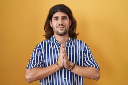 Photo for Hispanic man with long hair standing over yellow background begging and praying with hands together with hope expression on face very emotional and worried. begging. - Royalty Free Image