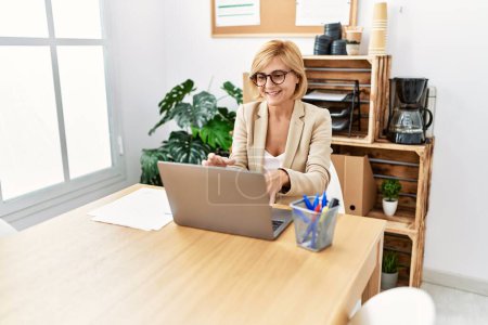 Foto de Middle age blonde woman smiling confident having video call at office - Imagen libre de derechos