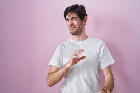 Photo for Young hispanic man standing over pink background disgusted expression, displeased and fearful doing disgust face because aversion reaction. - Royalty Free Image