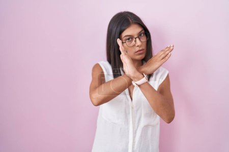 Téléchargez les photos : Brunette jeune femme debout sur fond rose portant des lunettes expression de rejet croisant les bras faisant signe négatif, visage en colère - en image libre de droit