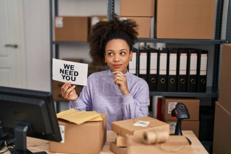 Foto de Young african american woman working at small business ecommerce holding banner serious face thinking about question with hand on chin, thoughtful about confusing idea - Imagen libre de derechos