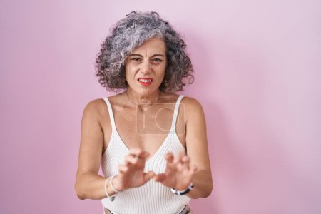 Photo for Middle age woman with grey hair standing over pink background disgusted expression, displeased and fearful doing disgust face because aversion reaction. - Royalty Free Image