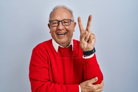 Photo for Senior man with grey hair standing over isolated background smiling with happy face winking at the camera doing victory sign with fingers. number two. - Royalty Free Image