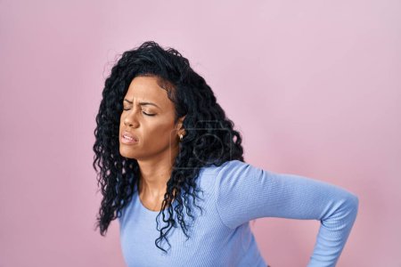Photo for Middle age hispanic woman standing over pink background suffering of backache, touching back with hand, muscular pain - Royalty Free Image