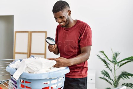 Photo for Young african american man smiling confident looking clothes using loupe at laundry room - Royalty Free Image