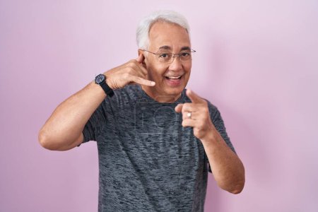 Photo for Middle age man with grey hair standing over pink background smiling doing talking on the telephone gesture and pointing to you. call me. - Royalty Free Image