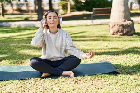 Téléchargez les photos : Femme d'âge moyen faisant de l'exercice de yoga assis sur l'herbe au parc - en image libre de droit