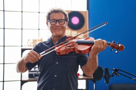 Foto de Hombre de mediana edad músico sonriendo confiado tocando el violín en el estudio de música - Imagen libre de derechos