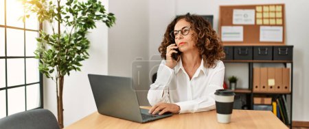 Foto de Mujer hispana madura trabajando hablando por teléfono en la oficina - Imagen libre de derechos