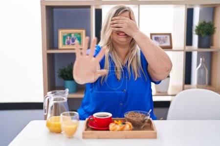 Photo for Caucasian plus size woman eating breakfast at home covering eyes with hands and doing stop gesture with sad and fear expression. embarrassed and negative concept. - Royalty Free Image