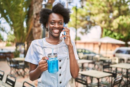 Téléchargez les photos : Young african woman talking to the phone holding bottle at street - en image libre de droit