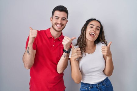Photo for Young hispanic couple standing over isolated background success sign doing positive gesture with hand, thumbs up smiling and happy. cheerful expression and winner gesture. - Royalty Free Image