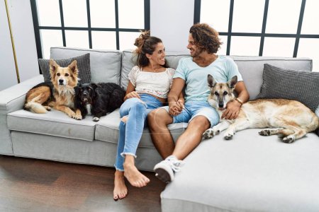Téléchargez les photos : Homme et femme couple souriant confiant assis sur le canapé avec des chiens à la maison - en image libre de droit