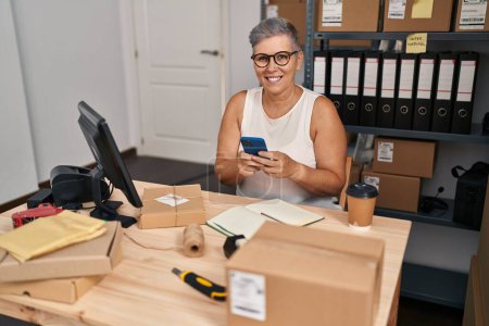 Téléchargez les photos : Middle age woman ecommerce business worker using smartphone at office - en image libre de droit