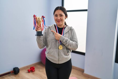 Photo for Young latin woman holding winner trophy smiling happy pointing with hand and finger - Royalty Free Image