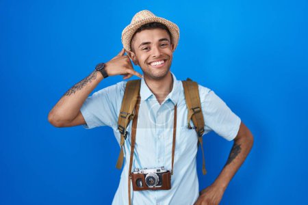 Photo for Brazilian young man holding vintage camera smiling doing phone gesture with hand and fingers like talking on the telephone. communicating concepts. - Royalty Free Image