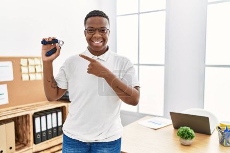 Téléchargez les photos : Jeune homme africain entraînement musculaire avec poignée de main au bureau souriant heureux pointage avec la main et le doigt - en image libre de droit
