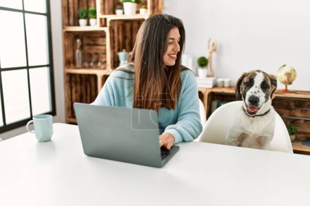Photo for Young woman using laptop sitting on table with dog at home - Royalty Free Image
