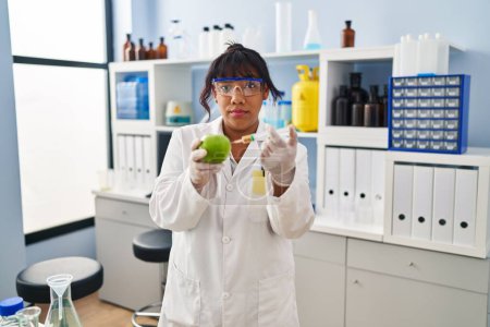 Foto de Hispanic woman working at scientist laboratory with apple skeptic and nervous, frowning upset because of problem. negative person. - Imagen libre de derechos