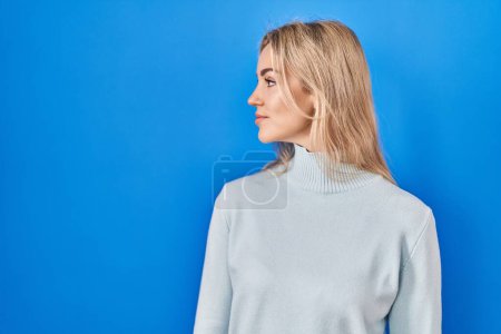 Photo for Young caucasian woman standing over blue background looking to side, relax profile pose with natural face with confident smile. - Royalty Free Image