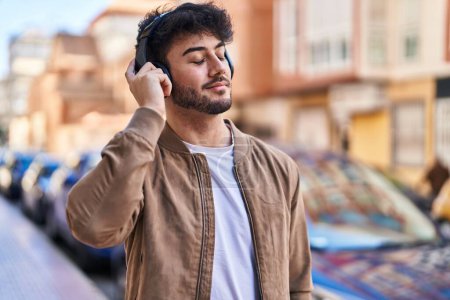 Téléchargez les photos : Jeune homme hispanique souriant confiant écoutant de la musique dans la rue - en image libre de droit
