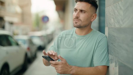 Photo for Young hispanic man using smartphone with serious expression at street - Royalty Free Image